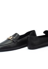 Mocasines de cuero negro con punta afilada, que cuentan con una banda decorativa en tono dorado a lo largo del empeine y una suela plana de goma.