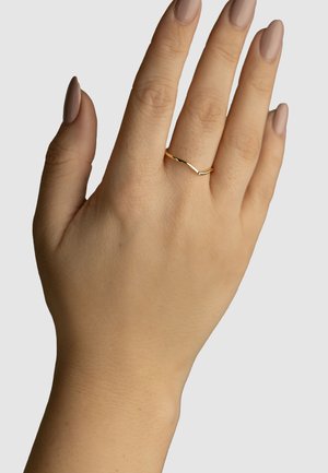 Goldring mit Chevron-Design, schmale Band, glatte Textur, getragen an einer Hand mit mittlerem Hautton und gepflegten Nägeln.