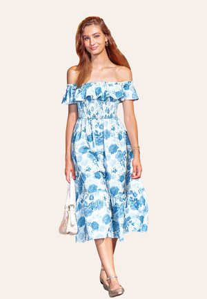 Abito blu floreale a spalle scoperte con scollatura arricciata, corpino elasticizzato e gonna fluente. Accessoriato con una borsa bianca e scarpe argentate.