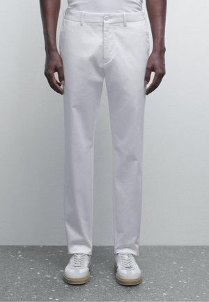 White cotton trousers with a straight cut, featuring a flat front and side pockets, paired with white and beige sneakers.