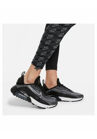 Czarno-szare sneakersy Nike z siateczkową cholewką, wyraźnym amortyzatorem Air Max oraz teksturowymi detalami. Uzupełnione czarnymi legginsami z powtarzającym się logo.