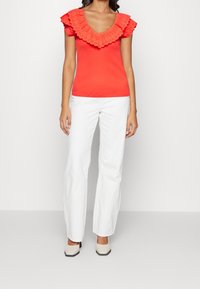 Röd kortärmad topp med en stor scallop-lace krage, tillsammans med vita raka byxor och ljusa klackskor med blockklack.