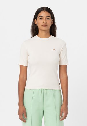 Lys cremefarvet kortærmet ribbet t-shirt med rund hals og lille broderet logo på brystet. Glat tekstur, tætsiddende silhuet.