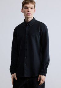 Sötét tengerészkék, gombos ing, texturált felülettel, klasszikus gallérral, hosszú ujjakkal és finom logóhímzéssel a mellrészen.