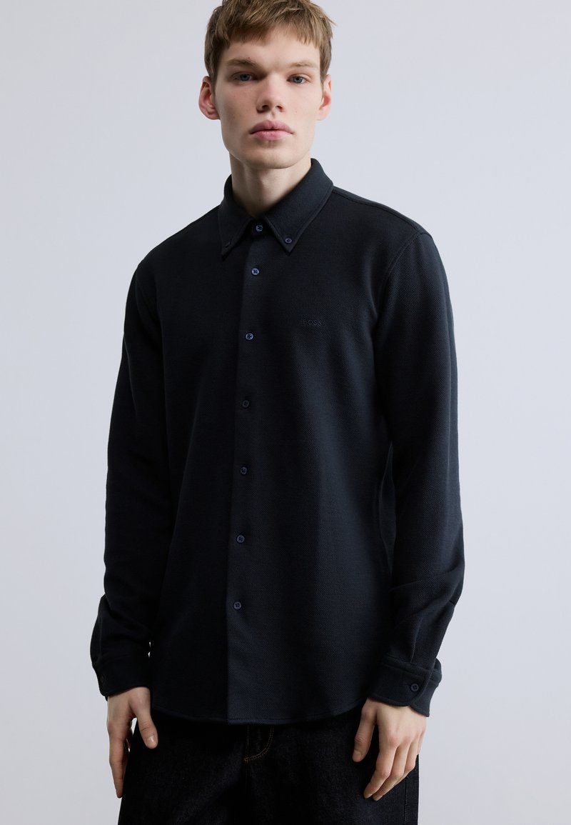 Sötét tengerészkék, gombos ing, texturált felülettel, klasszikus gallérral, hosszú ujjakkal és finom logóhímzéssel a mellrészen.