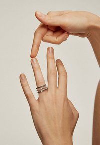 Anillo multi-banda de plata con acentos negros, exhibido en los dedos. Acabado suave, diseño geométrico y bandas entrelazadas que crean textura.