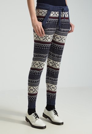 Leggings met marineblauwe, crèmekleurige en bordeauxkleurige Noorse patronen, geribbelde marineblauwe tailleband en manchetten, gedragen met zwarte sokken en witte veterschoenen.