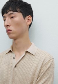 Beige strikket polo t-shirt med et struktureret mønster, der har en kravehals og to knapper. Glat stof, afslappet pasform.