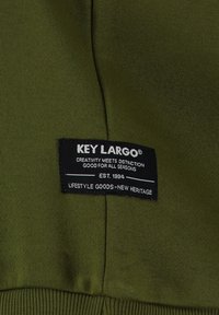 Tessuto verde oliva con una texture liscia presenta un'etichetta nera cucita con la scritta "KEY LARGO" e dettagli in testo bianco.