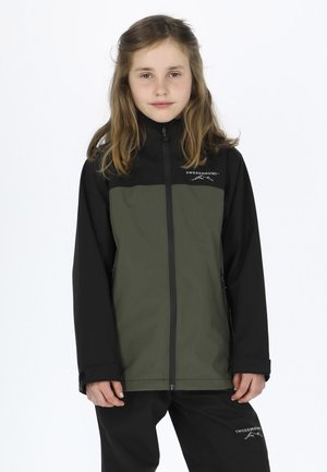 Grüne und schwarze Softshell-Jacke mit Reißverschluss vorne, hohem Kragen und Logo, kombiniert mit schwarzen Hosen. Glatte Textur, lässige Passform.