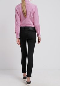 Černé skinny džíny v kombinaci s růžovou a bílou pruhovanou košilí s dlouhým rukávem. Má volný střih a viditelné zadní kapsy.