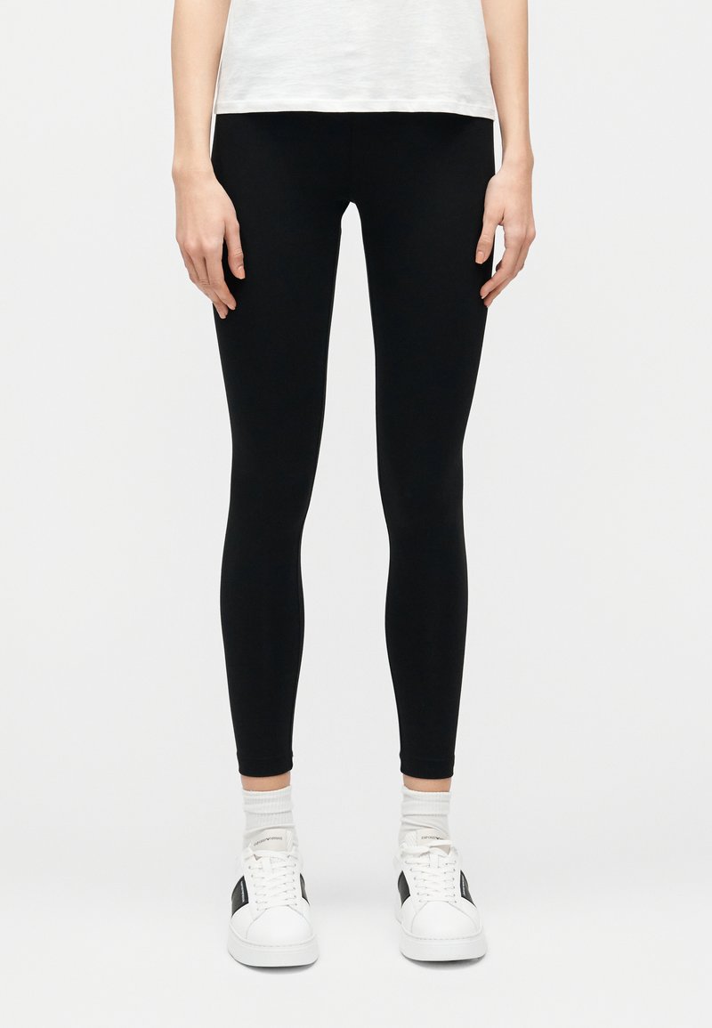 Leggings nere con una texture liscia ed elastica, design aderente e vita alta, abbinati a sneaker bianche e calzini sportivi bianchi.