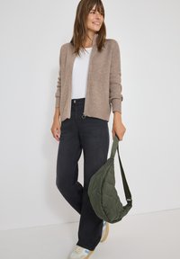 Beige ribbad kofta, vit t-shirt, svarta jeans, grön kviltad axelväska, krämfärgade sneakers med blå accenter. Släta texturer, avslappnad passform.
