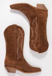 Brune ruskind cowboystøvler med hvide broderede detaljer, spids tå og stablet hæl. Har en trække-flap bagpå.