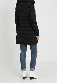 Musta toppatakki hupulla, vetoketjullinen edessä ja joustavat hihansuut. Yhdistetty sinisiin farkkuihin ja valkoisiin nilkkureihin. Suora siluetti.