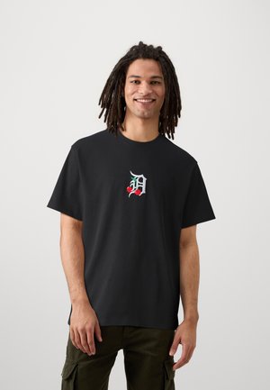 Camiseta de algodón negra con un colorido logotipo bordado de cerezas. Manga corta y corte relajado, combinada con pantalones cargo verde oliva.