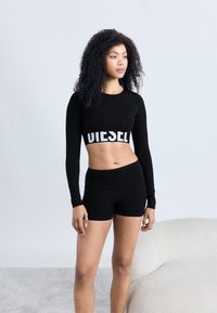 Must pikkade varrukatega lühike topp, millel on suured valged sõnad "DIESEL" ja sobivad mustad lühikesed püksid, valmistatud siledast materjalist ning vormitud lõikega.