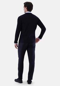 Dunkelblauer, taillierter Pullover mit langen Ärmeln, Rundhalsausschnitt und subtiler Textur, kombiniert mit passenden dunklen Hosen und schwarzen Schuhen.