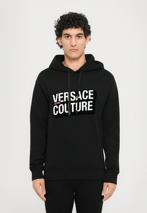 Zwarte hoodie van sweaterstof, met een witte grafische print "VERSACE JEANS COUTURE" op de voorkant. Klassiek ontwerp met een capuchon met koord.