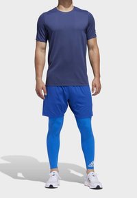 Námořnické sportovní tričko s krátkým rukávem, modré kraťasy a modré legíny s bílým logem, doplněné bílými sportovními botami.