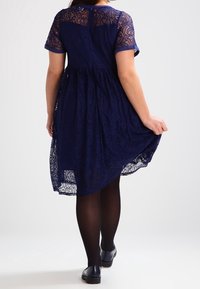 Abito in pizzo blu navy con maniche corte, pattern testurizzati e gonna svasata. Completato da collant opachi neri e scarpe basse.