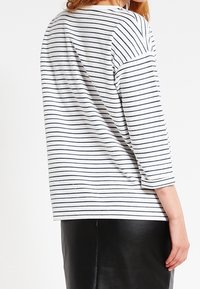 Gestreepte lange mouwen top in wit en marineblauw, met een ontspannen pasvorm en een ronde halslijn, gedragen met een zwarte leren rok.