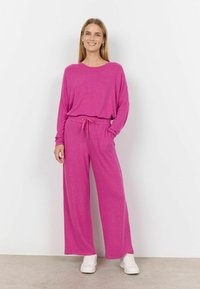 Rúžové loungewear súpravy, ktoré sa skladajú z voľnej dlhovej blúzky a širokých nohavíc s nastaviteľným šnúrkovým pásom. Hladká textura, mäkká látka.