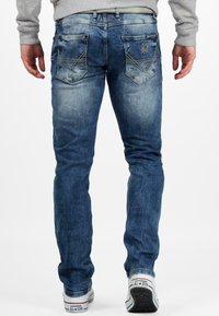 Mannen's vervaagde blauwe denim jeans met een slim fit, met twee achterzakken met decoratieve stiksels en geborduurd logo detail.