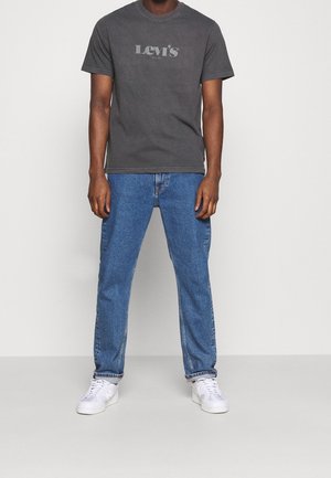 T-shirt in cotone grigia con logo Levi's stampato, abbinata a jeans in denim blu e sneaker bianche, con una vestibilità rilassata e un design essenziale.