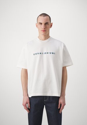 T-shirt en coton blanc avec des manches courtes, un col rond et un texte brodé "TOUS LES JOURS JE PORTE SUNNE" en bleu et vert.