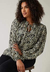 Bluse med blomsterprint i sort og creme, featuring en bindebånd i halsen, lange ærmer med elastiske manchetter og en afslappet pasform.