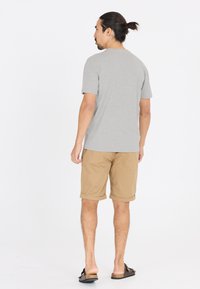 Harmaa lyhythihainen t-paita yhdistettynä khaki-shortsien kanssa, joissa on käännetyt helmatt. Asusteena ruskeat sandaalit, jotka luovat rentoa ilmettä takaa katsottuna.