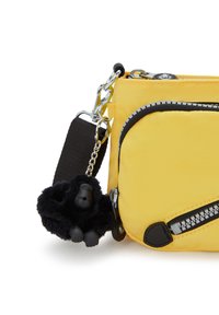 Keltainen nylonsuojagalleria, jossa on mustat vetoketjakiinnikkeet, irrotettava musta karvainen gorillaherkkukkeytin ja säädettävä musta hihna.