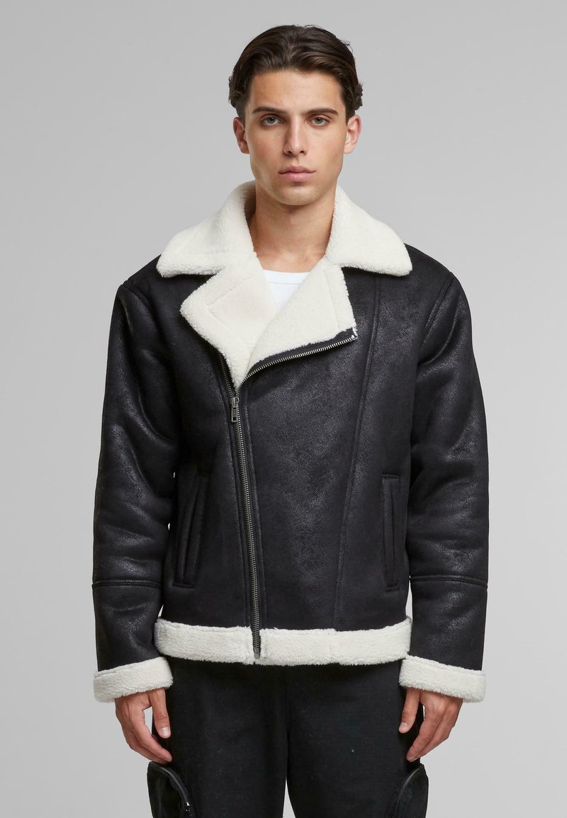 Chaqueta de piel sintética negra con cuello y puños de piel sintética blanca, con cierre frontal de cremallera y dos bolsillos laterales. Textura suave, diseño casual.