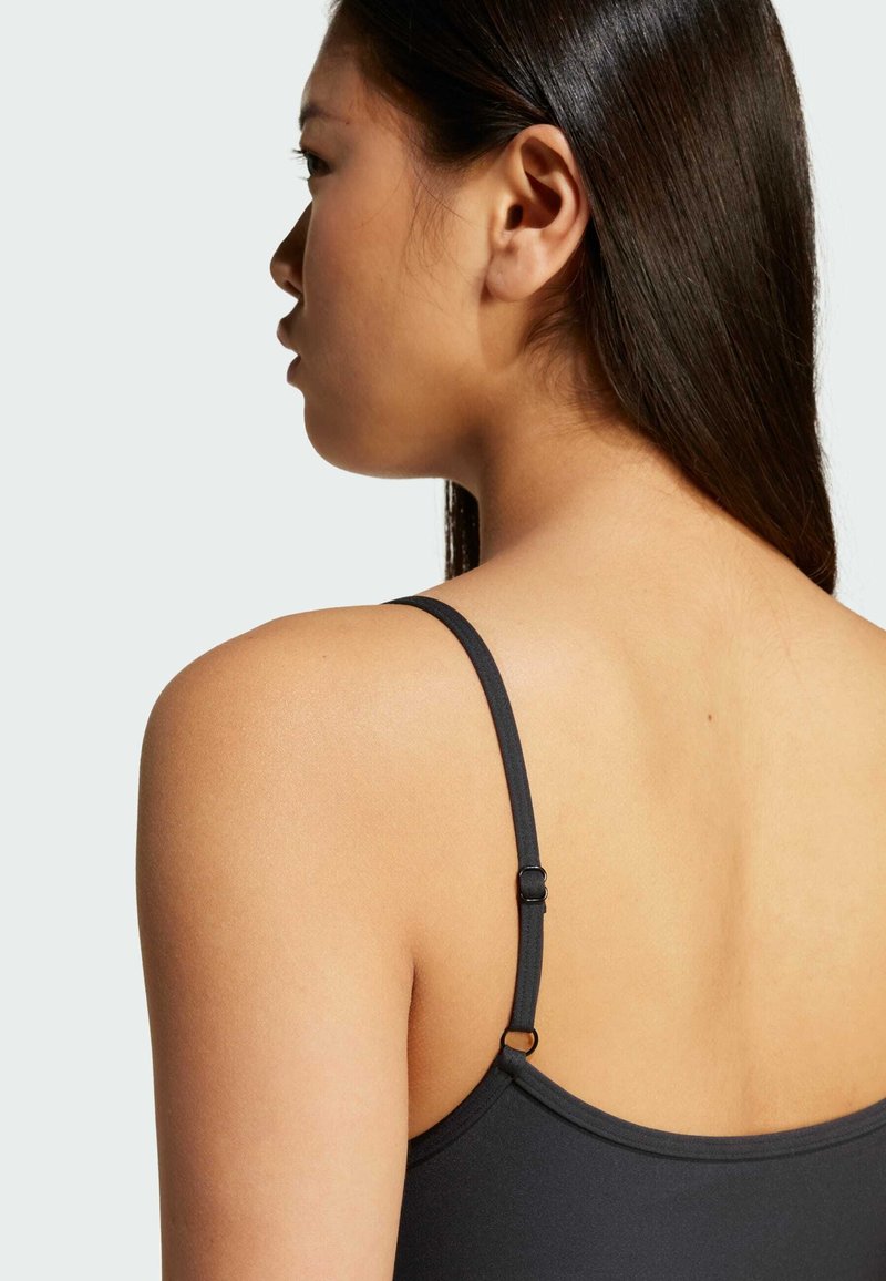 Reggiseno nero con spalline sottili, texture morbida, elementi regolabili e un design semplice, posizionato sulla spalla e sulla schiena di un modello.