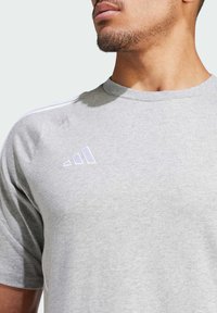 Grijze T-shirt gemaakt van zachte stof, met korte mouwen, een ronde hals en witte adidas-logo accenten op de borst en schouders.