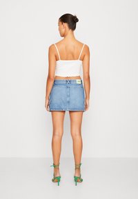 Denim mini-jurk met een strakke pasvorm, lichtblauwe kleur en zijzakken; gecombineerd met een witte cropped top en groene hoge hakken.