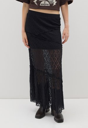 Gonna maxi nera in pizzo con design a strati, texture semi-trasparente e vita elasticizzata. Abbinata a stivaletti neri alla caviglia.