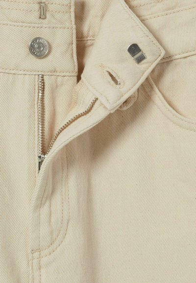 Pantalones beige de mezcla de algodón que presentan un zipper plateado, cierre de botón y detalles de costura. La tela tiene una apariencia texturada y acanalada.