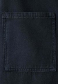 Gros plan d'une poche carrée en tissu bleu foncé cousue avec des coutures visibles sur un vêtement.