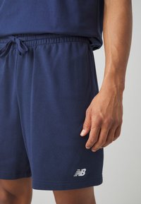Pantaloni corti in cotone blu con cintura elastica, cordoncino e logo silver New Balance sull'orlo sinistro in basso. Morbido al tatto e vestibilità comoda.