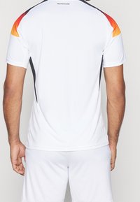 Bílé sportovní tričko s krátkými rukávy a černými bočními akcenty. Na zádech je přechodový design v červené a žluté barvě na ramenech.