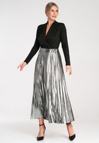 Czarny top z długim rękawem w białe kropki, zestawiony z srebrną plisowaną spódnicą maxi. Spódnica ma błyszczące wykończenie i szeroki pasek w talii.
