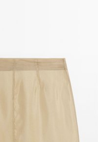 Beige skirt with a smooth, matte texture and a fitted waist. Features clean lines and subtle stitching details, designed for a minimalist look.