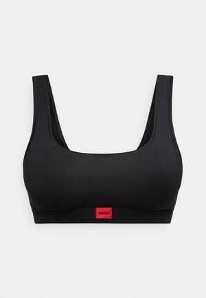 Μαύρο αθλητικό σουτιέν χωρίς ραφές με πλατιές τιράντες και μια μικρή κόκκινη ετικέτα με την επιγραφή "HUGO" στο κέντρο της κάτω ταινίας, πάνω σε λευκό φόντο.