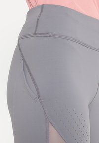 Hochtaillierte graue Leggings aus einem glatten, dehnbaren Material mit Seitentaschen und durchlässigen Akzenten am Saum für Atmungsaktivität.