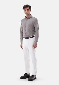 Camicia grigia a maniche lunghe con bottoni, pantaloni bianchi, cintura nera e scarpe stringate nere, caratterizzati da un tessuto liscio e una vestibilità su misura.
