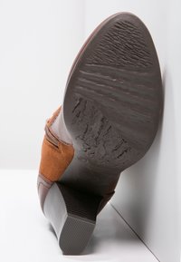 Bottine marron avec une combinaison de textures lisses et en daim, un talon incliné et une semelle en caoutchouc texturé. Montre un motif d'usure sur la semelle.