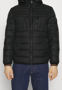 Czarna pikowana kurtka z zamkiem z przodu, wyposażona w odpinany kaptur, teksturowane panele oraz kontrastujące pomarańczowe akcenty na mankietach.