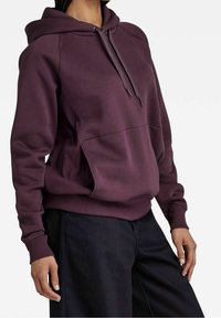 Felpa bordeaux con cappuccio e cordino, tasca frontale e polsini a coste; realizzata in tessuto morbido e texturizzato; fessure laterali per facilità di movimento.